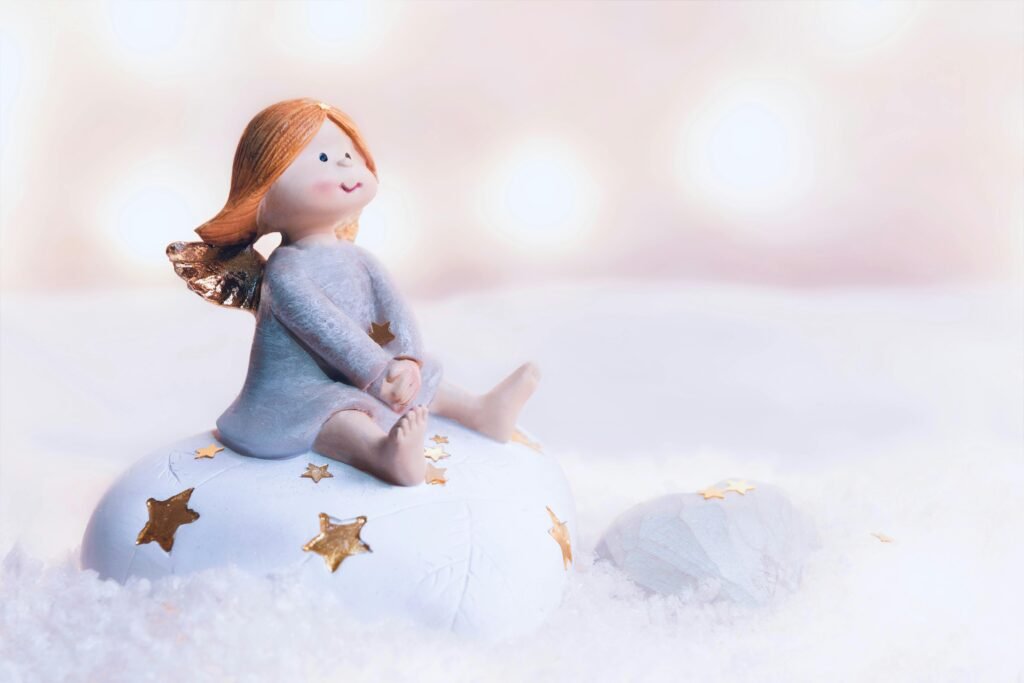 Cute angel figurine with red hair sitting on snow adorned with golden stars, exuding a whimsical winter charm.
