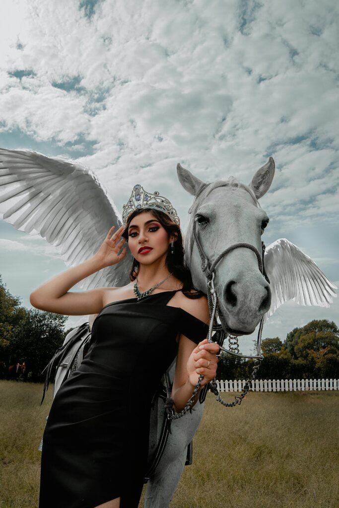 A woman in a black dress poses with a winged horse under a cloudy sky.