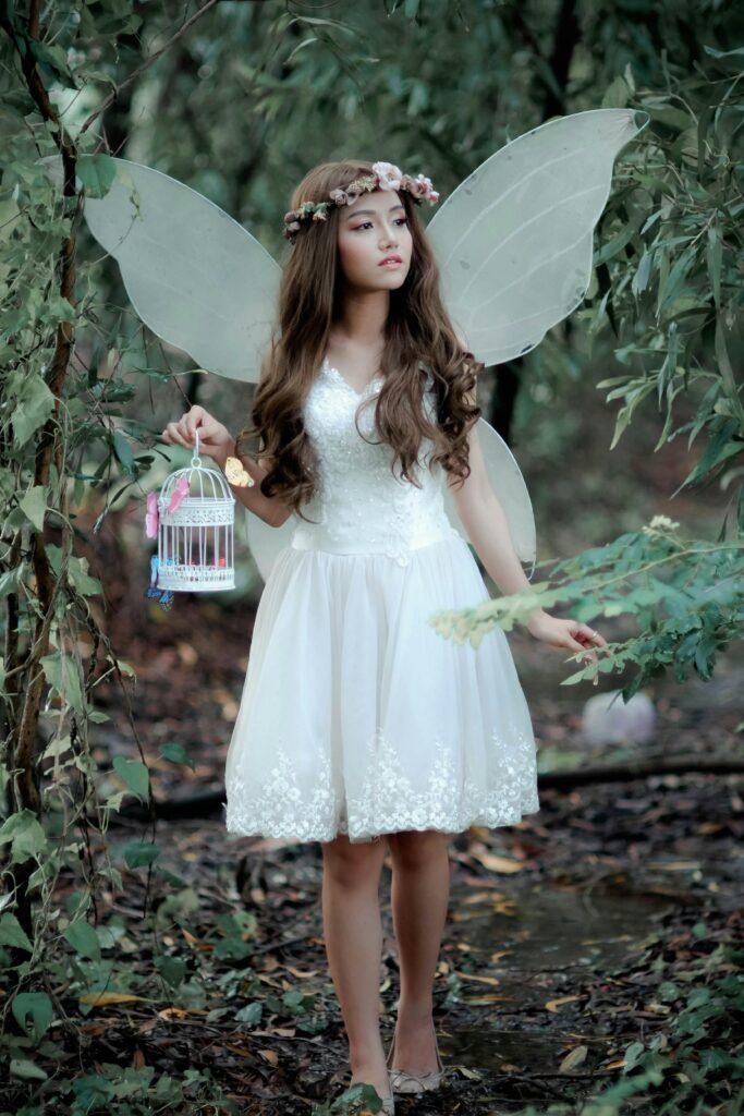 Fairy in mystical forest wearing a white dress and wings, holding a decorative birdcage.