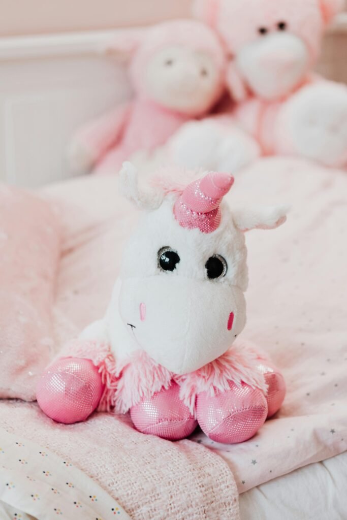 Adorable pink unicorn stuffed toy on a child's bed with plush animals in the background.